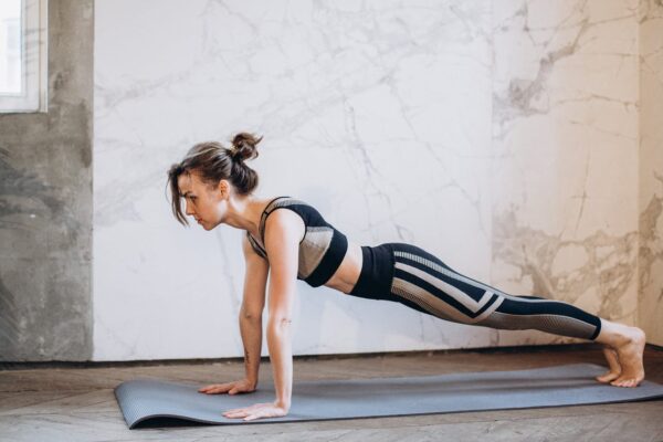 A woman performing a plank pose on a yoga mat indoors, showcasing strength and focus.