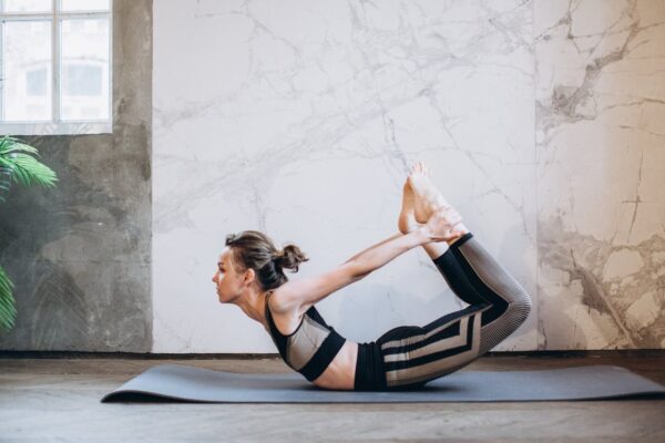 A woman performing the bow pose in a serene indoor setting, emphasizing fitness and mindfulness.