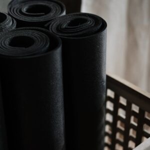 Close-up view of black yoga mats rolled and stacked in a wooden basket indoors.