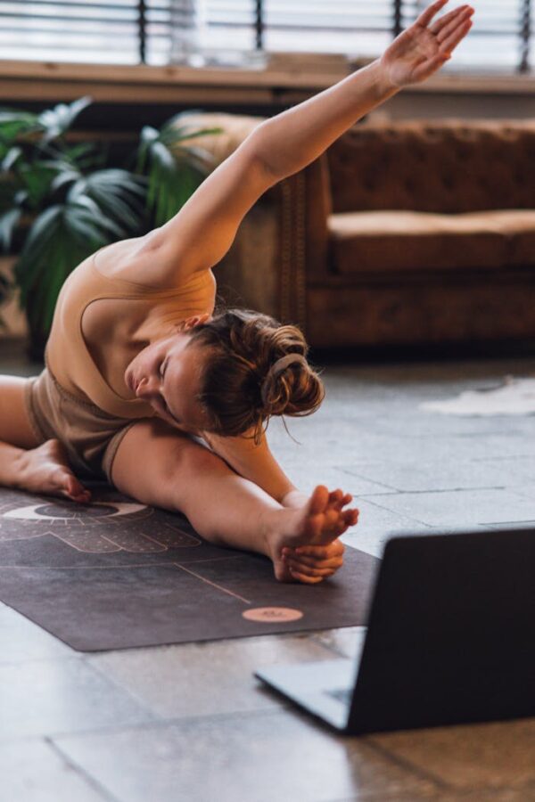 A woman engaged in a yoga session on a mat in a cozy living room setting, aided by a laptop.