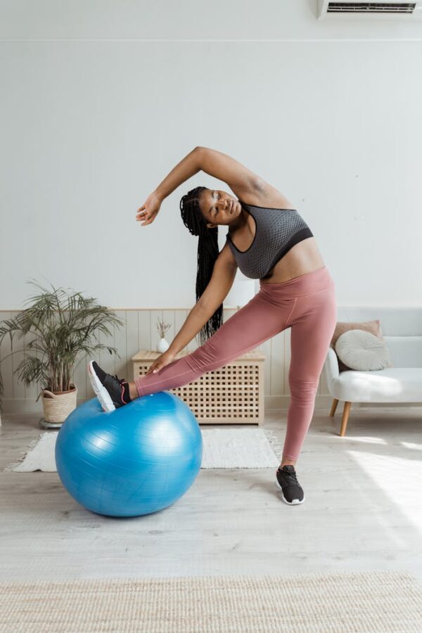 Plus-size woman in activewear stretching with a blue fitness ball indoors.
